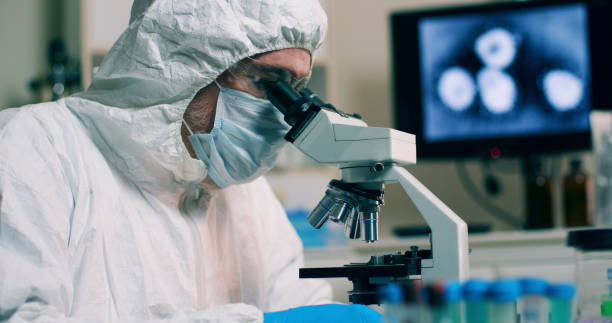 um cientista de pesquisa trabalhando em seu laboratório com uma amostra ou espécime e uma imagem do wuhan coronavirus exibida em uma tela de computador. - specimen holder fotos - fotografias e filmes do acervo