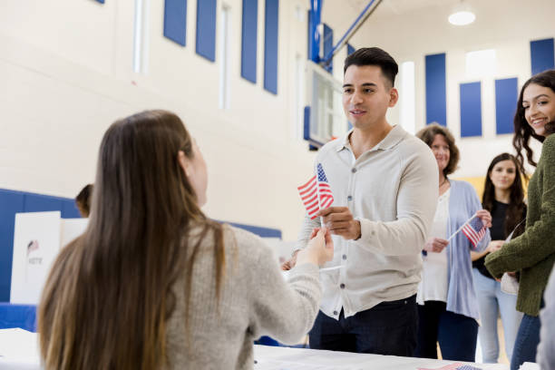 istock Unrecognizable polling place volunteer gives man flag 1203196304