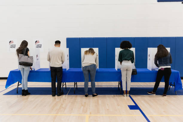 Rear view photo five people casting ballots A rear view of a multi-ethnic group of people casting their ballots in the election. presidential election photos stock pictures, royalty-free photos & images