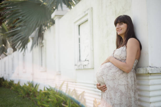 Pregnant woman standing near the wall and caresses her belly Image of happy pregnant woman touching her big belly. Happy pregnant European woman with big tummy is relaxing. Pregnancy, motherhood, people and expectation concept. Complete family. olivia mum stock pictures, royalty-free photos & images