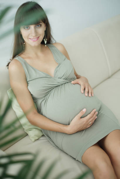 Smiling pregnant woman expecting child sitting on the sofa and caressing her belly Image of happy pregnant woman touching her big belly. Happy pregnant European woman with big tummy is relaxing. Pregnancy, motherhood, people and expectation concept. Complete family. olivia mum stock pictures, royalty-free photos & images