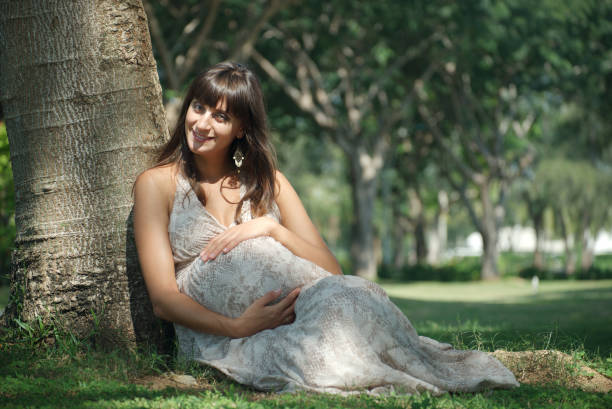 Happy and smile pregnant woman siting on the lawn and touching her big belly Image of happy pregnant woman touching her big belly. Happy pregnant European woman with big tummy is relaxing. Pregnancy, motherhood, people and expectation concept. Complete family. olivia mum stock pictures, royalty-free photos & images