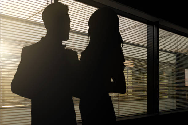 Couple romancing at work Concept image of romance at work - silhouettes of a woman and a man hugging each other in a dark corporate office work romance stock pictures, royalty-free photos & images