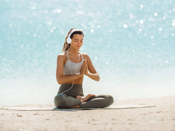mujer en yoga meditation pose con auriculares en la playa - relaxation exercise audio fotografías e imágenes de stock