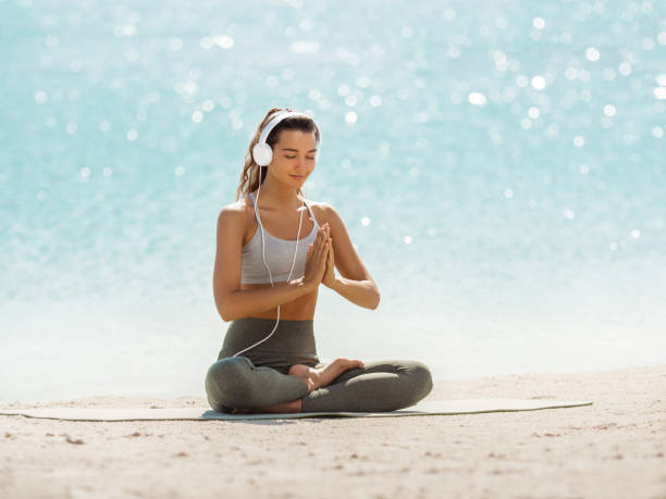 mulher em yoga meditação pose com fones de ouvido na praia - creative thinking audio - fotografias e filmes do acervo