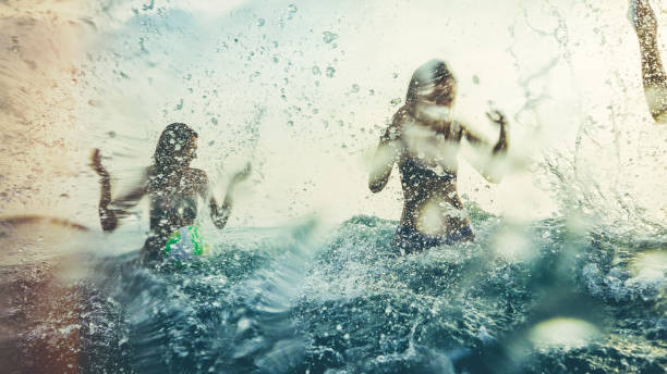 amis jouant ensemble dans la mer, éclaboussures et plongeant pendant un coucher du soleil d'été - vague déferlante photos photos et images de collection