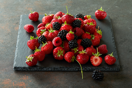 Heap of strawberries, raspberries and blackberries on a piece of slate.
