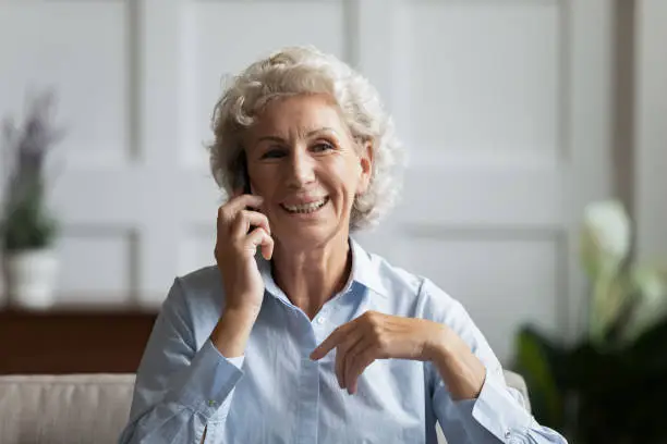 Head shot smiling middle aged woman talking on phone with friends. Happy mature older grandmother chatting with grownup children grandchildren. Satisfied elderly client ordering delivery food or taxi.