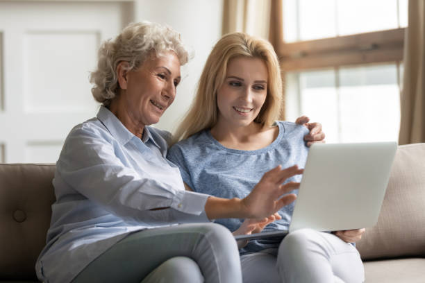 istock Happy young woman teaching elderly mother use applications on laptop. 1203214400