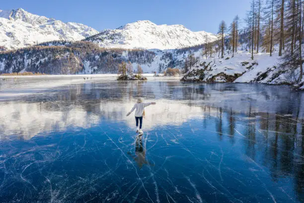Aerial view of Young woman ice skating on frozen lake at sunset having fun and enjoying winter vacations