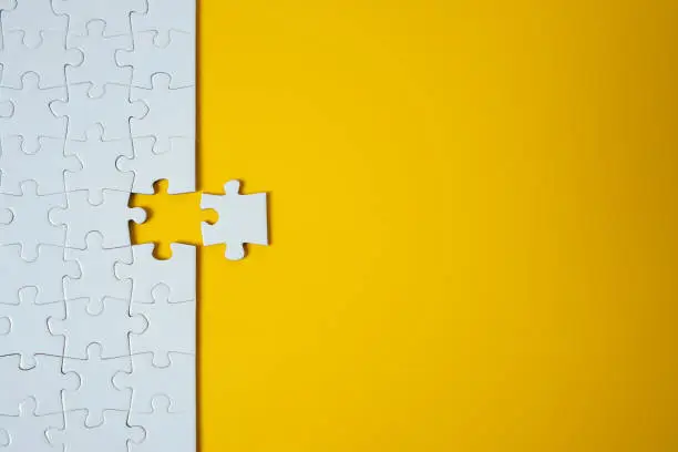 White jigsaw puzzle on yellow background. Team business success partnership or teamwork.