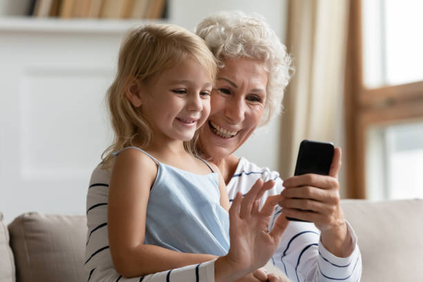 mature woman showing funny mobile apps to small kid girl. - wireless technology cheerful granddaughter grandmother imagens e fotografias de stock