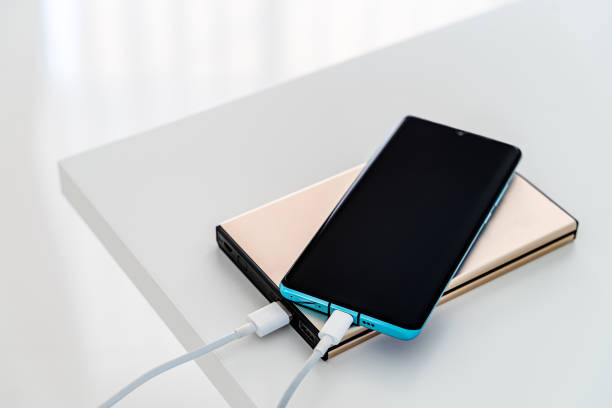 istock Mobile phone connected to charger power bank on white table. 1203220233
