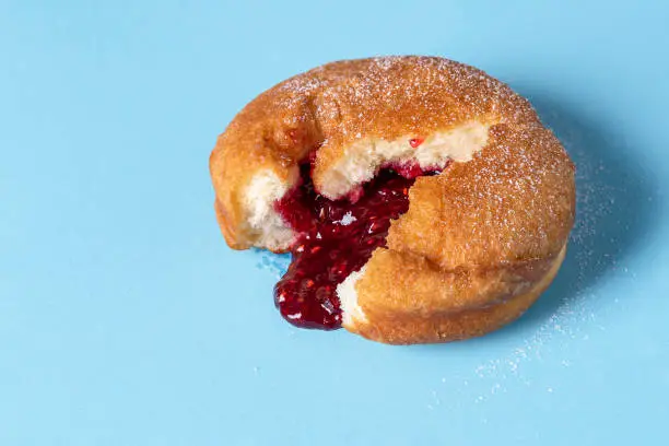 German Berliner doughnut with raspberry jam filling on a blue seamless background. Macro image of a donut with jam. Homemade dessert. Famous sweets.