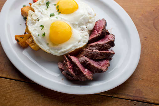 Steak and eggs, Traditional classical American or French Bistro brunch item. Steak, served medium raw with sunny side up eggs and fried potato hash