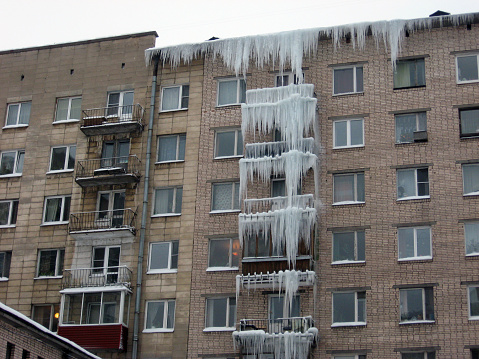 Huge icicles hang from the balconies of a residential building. Harsh winter. Utilities do not cope. Dangerous stalactites. Terrible ice in the big city.