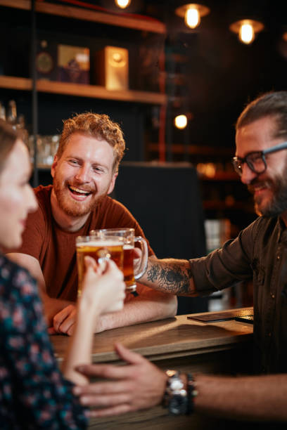 amici in piedi al bar e tostati con birra. - vertical caucasian glasses red hair foto e immagini stock