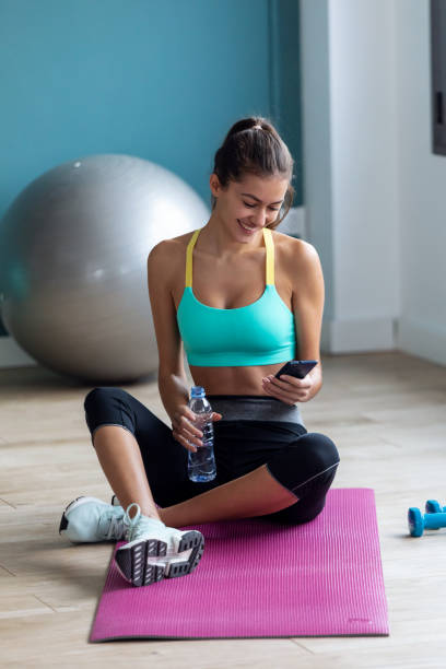 istock Sporty young woman using her mobile phone while holding water bottle after a pilates class on the gym. 1203229204