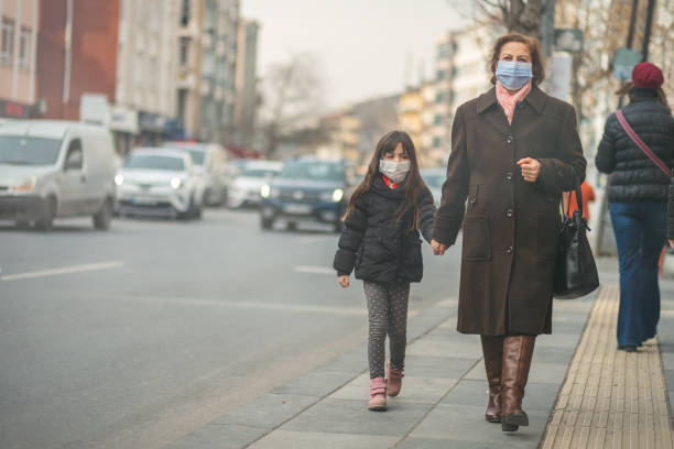 donna sta andando al lavoro.indossa maschera n95.prevenire polvere pm2.5 e smog, madre e bambino che indossano una maschera per proteggere il proprio bambino dall'inquinamento atmosferico e dalle malattie infettive - global warming smog city pollution foto e immagini stock