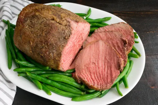 Sliced medium rare roasted beef eye of round on a platter of green beans