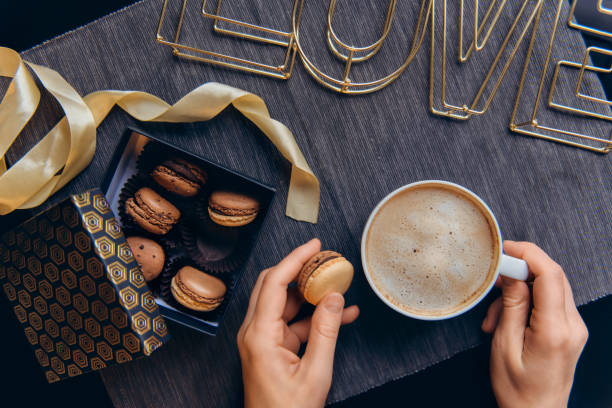 istock Top view female hands with coffee cup and macaron cake. Romantic breakfast for lover. Noir nordic style. Box with sweets and wire word Love on gray napkin on black table. Hygge Valentine's day concept 1203235174