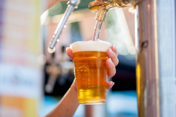 beer is poured into a glass from a tap. The bartender pours beer into a plastic glass stock photo