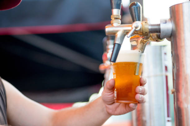 istock beer is poured into a glass from a tap. The bartender pours beer into a plastic glass 1203237663
