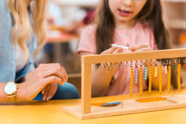 Selective focus of kid playing wooden game by teacher in montessori school, cropped view Selective focus of kid playing wooden game by teacher in montessori school, cropped view montessori education stock pictures, royalty-free photos & images