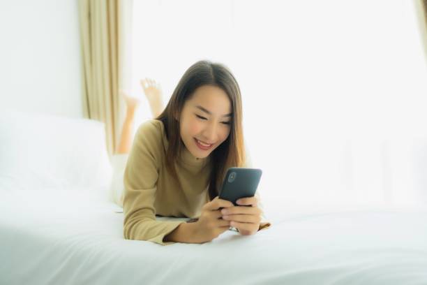 istock Young asian woman using mobile smart phone on bed 1203258584