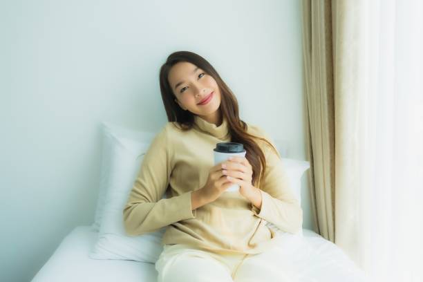 istock Young asian woman with coffee cup on bed 1203259419