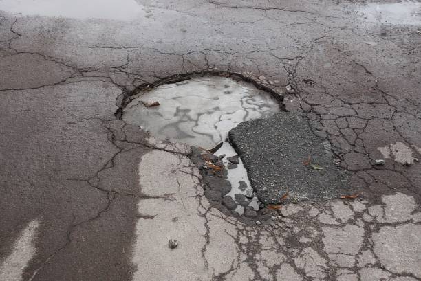 istock one large pothole with white ice on a gray asphalt road with cracks 1203260422
