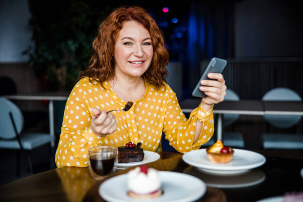 istock Smiling lady enjoying cake and using cellphone in cafe 1203264530