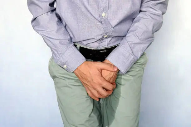 Urinary incontinence concept. Wet person. Blue background. adult man holds hands the groin area and trousers wet from urine. Health problem. Medical concept.