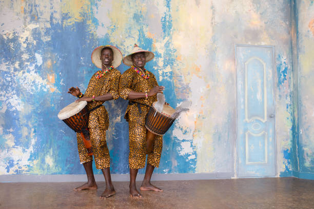 eine gruppe von menschen in traditionellen afrikanischen kostümen spielen jembe trommeln - traditional song stock-fotos und bilder