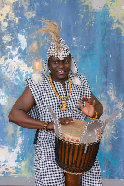 African artist in traditional clothes playing djembe drum.