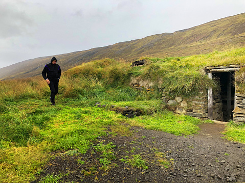 North Iceland: A tourist exploring an abandoned roadside turf home. Shot Near Seydisfjordur.
