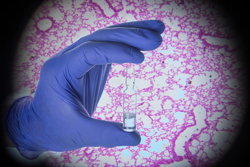 vaccine hold by glove with lung biopsy in background