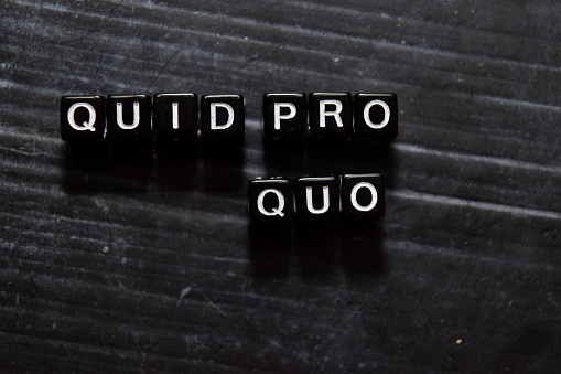 Quid Pro Quo in Latin on wooden cubes. On table background