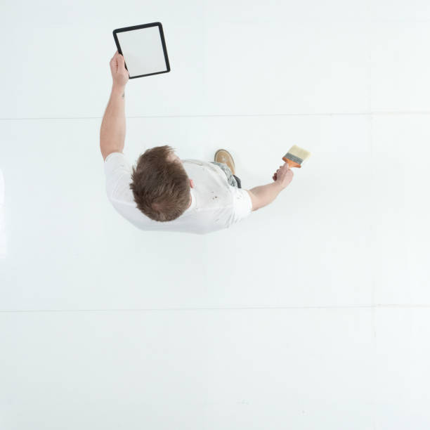 istock Caucasian young male painter standing wearing uniform and holding paintbrush and using touch screen 1203304532