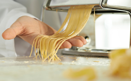 Hands of man making some Italian tagliatelle with pasta machine.