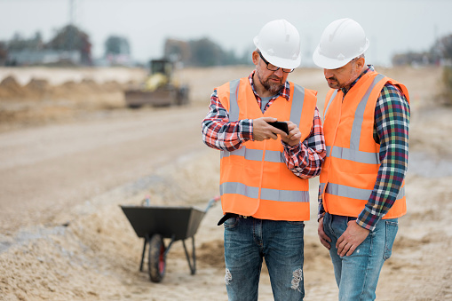 Dos constructores revisando el plan de construcción de carreteras por teléfono photo
