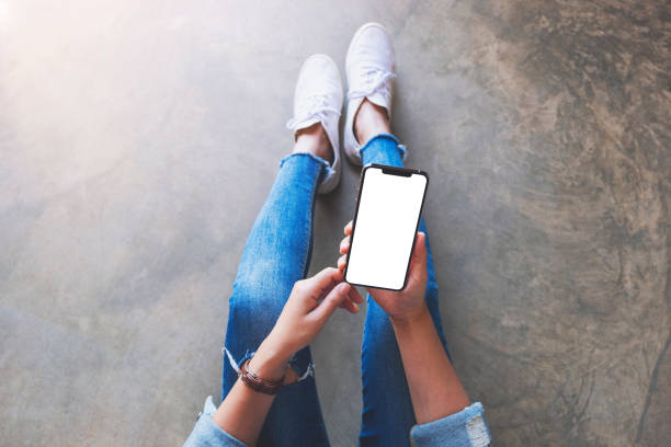 istock a woman holding black mobile phone with blank white screen while sitting on the floor 1203321161