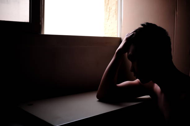 istock Sillhouette of a sad and problematic young man sitting next to a window light source. Mental health concept 1203323885