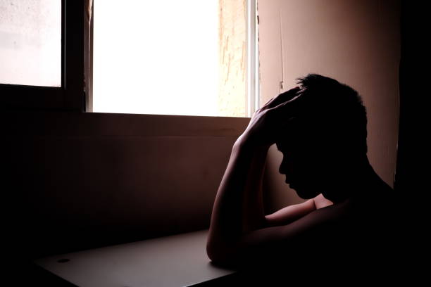 istock Sillhouette of a sad and problematic young man sitting next to a window light source. Mental health concept 1203323887
