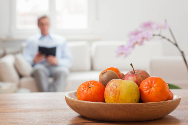 istock Man with e-book on a couch with fruit bowl in the foreground 1203325683