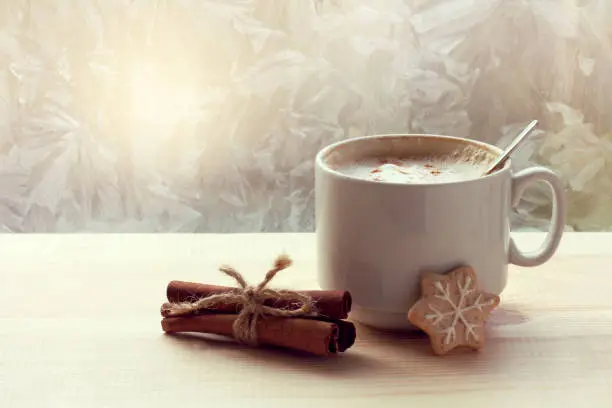 cup with coffee, cinnamon and cookies on the background of a window with frosty patterns