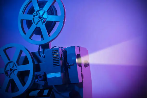 Vintage old fashioned projector in a dark room projecting a film on neon background