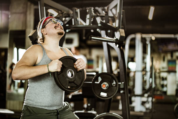istock Nerdy athletic man making an effort while exercising with barbell in a gym. 1203332113