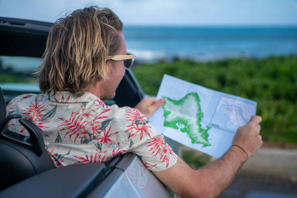 Young man inside convertible car looking at road map for directions