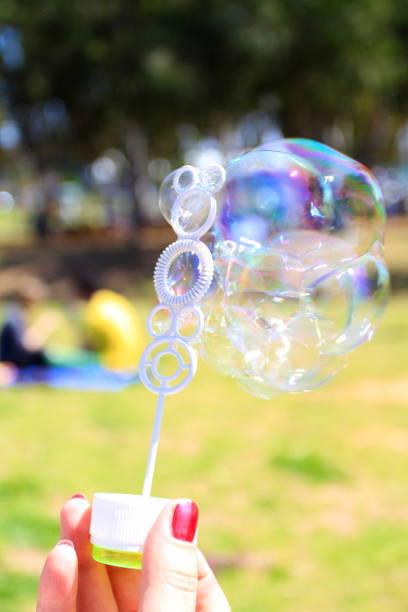 istock Female hand holding a wand for triggering Soap bubbles on green 1203340801